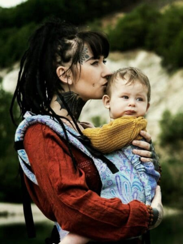 Almitra Tattva Marisa ergonomic baby carrier outdoors. Soft structured newborn-to-toddler baby carrier in breathable wool cashmere blend with pastel paisley print, padded shoulder straps, and supportive body panel, designed for hands-free parenting and inclusive, everyday babywearing comfort.