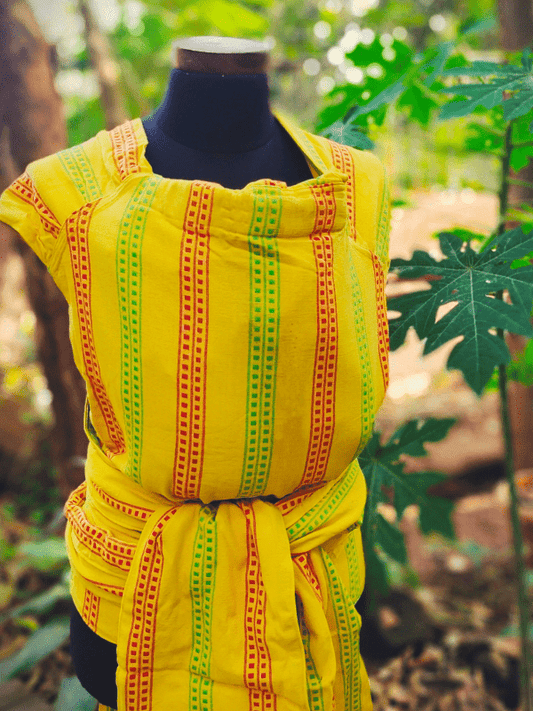 Front view of Almitra Tattva’s Nima wrap converted Meh Dai baby carrier in bright yellow with red and green striped pattern, styled on mannequin.