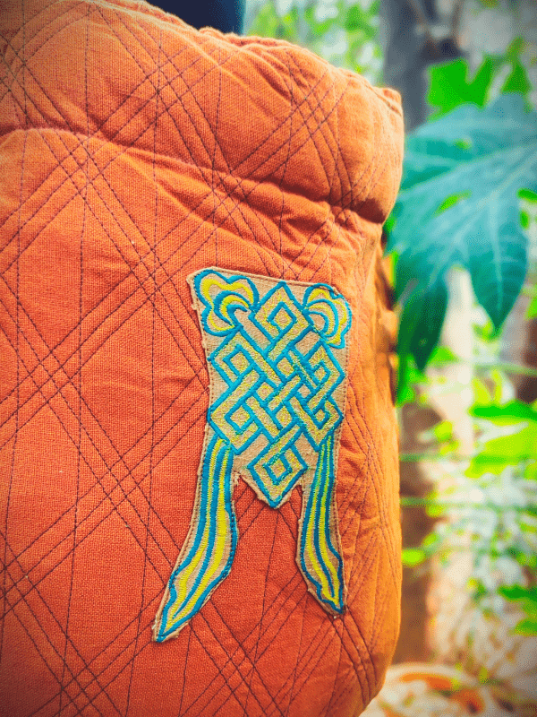Detailed embroidery of the eternal knot in teal and yellow on the back panel of the Agni Meh Dai wrap-converted baby carrier.
