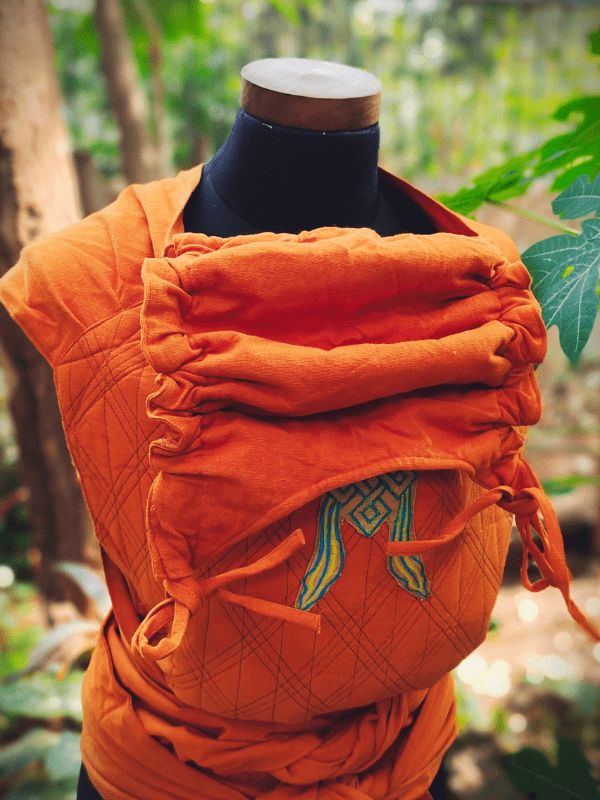 Frontal view of the Agni Meh Dai with adjustable wrap hood and pleated shoulders, styled on a mannequin against a forest backdrop.