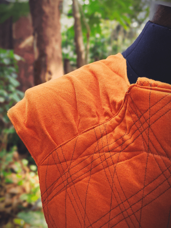 Close-up of pleated wrap-style shoulder on Agni Meh Dai baby carrier in burnt orange, showing textured cotton fabric and reinforced stitching