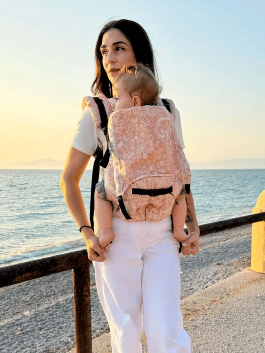 Mother carrying baby in the Almitra Tattva Tushara ergonomic baby carrier demonstrating a secure front carry with adjustable straps and breathable fabric.