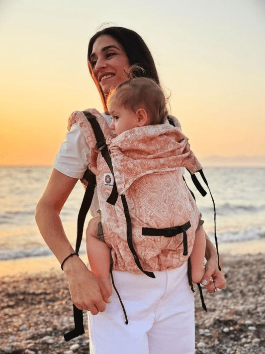 Close lifestyle view of a caregiver wearing the Almitra Tattva Tushara baby carrier with, designed for ergonomic babywearing with padded shoulder straps and breathable fabric.