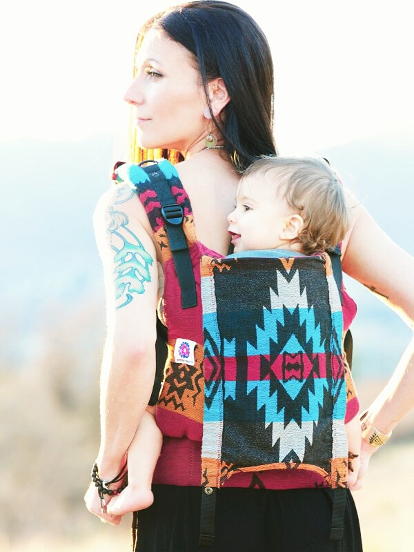 Back view of mother carrying toddler in the Almitra Tattva Auronee Yoga Baby Carrier, showcasing the detailed Kullu tribal geometric motifs and ergonomic structure.