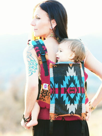 Back view of mother carrying toddler in the Almitra Tattva Auronee Yoga Baby Carrier, showcasing the detailed Kullu tribal geometric motifs and ergonomic structure.