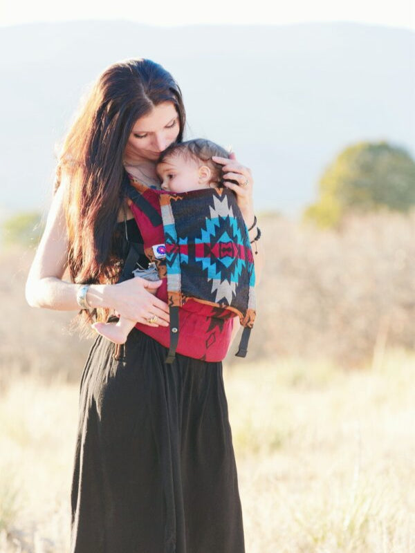 Mother wearing the Almitra Tattva Auronee Yoga Baby Carrier in Kullu design while front carrying her baby in an ergonomic and colorful geometric-patterned wrap-converted SSC.