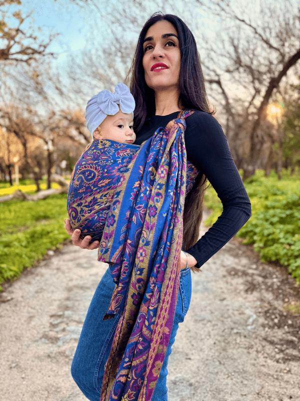 Ergonomic soft falak woven wrap baby carrier in blue paisley print, worn high on the caregiver’s torso with a newborn nestled securely, highlighting even weight distribution, adjustable wrap design, and conscious babywearing support.