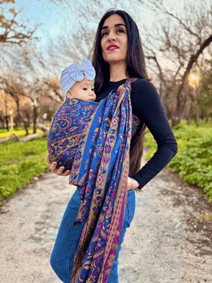 Ergonomic soft falak woven wrap baby carrier in blue paisley print, worn high on the caregiver’s torso with a newborn nestled securely, highlighting even weight distribution, adjustable wrap design, and conscious babywearing support.