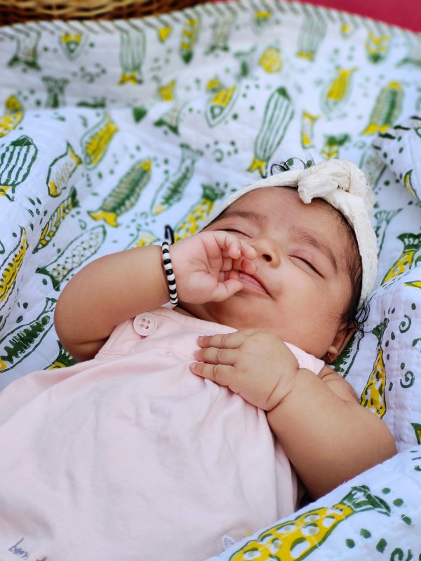 Baby peacefully resting on Almitra Tattva’s Fish Tales hand block printed muslin baby blanket, featuring green and yellow fish motifs on soft organic cotton.