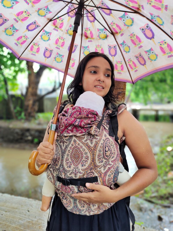 Caregiver wearing Ishkabon Yoga adjustable ergonomic baby carrier in paisley merino fabric, newborn supported in front carry position, breathable structured carrier designed for inclusive hands-free parenting