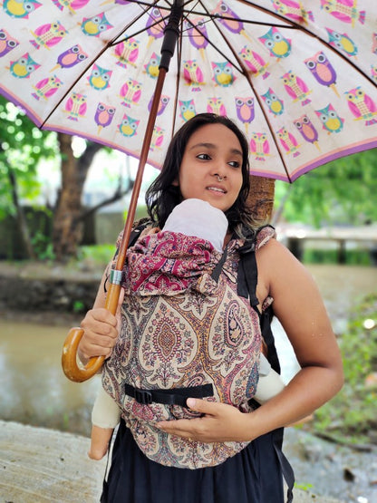 Caregiver wearing Ishkabon Yoga adjustable ergonomic baby carrier in paisley merino fabric, newborn supported in front carry position, breathable structured carrier designed for inclusive hands-free parenting