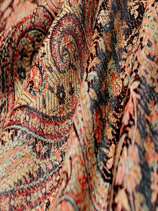 Detailed fabric view of Kalindi woven baby carrier wrap featuring dense paisley motifs in rust, black, and warm copper hues, highlighting textured weave designed for ergonomic support and hands-free parenting.
