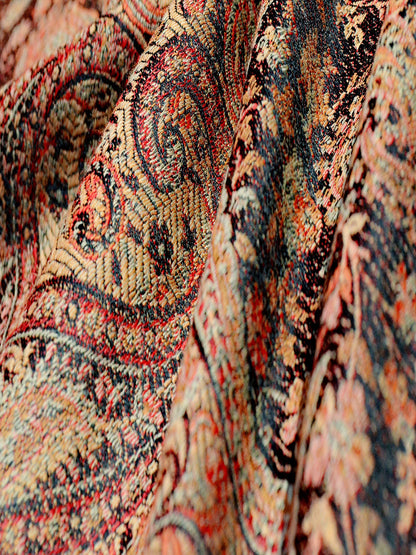 Detailed fabric view of Kalindi woven baby carrier wrap featuring dense paisley motifs in rust, black, and warm copper hues, highlighting textured weave designed for ergonomic support and hands-free parenting.