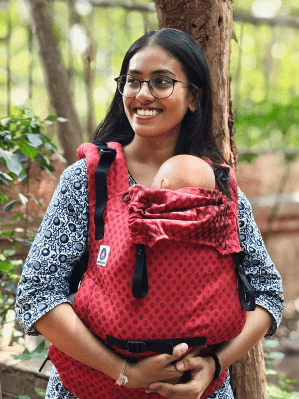 Mangalmay Sunrise ergonomic baby carrier in bold red cotton, with newborn nestled close, showcasing adjustable straps, supportive waistband, and breathable cotton design for everyday babywearing and gender-fluid caregiving.