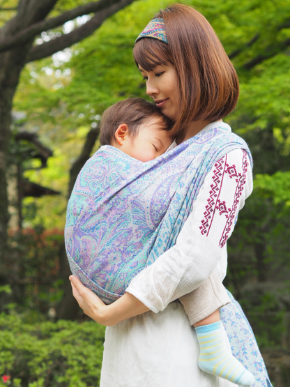 Woman holding a baby in a Marisa White Woven Wrap - Cashmere Collection outdoors with greenery in the background