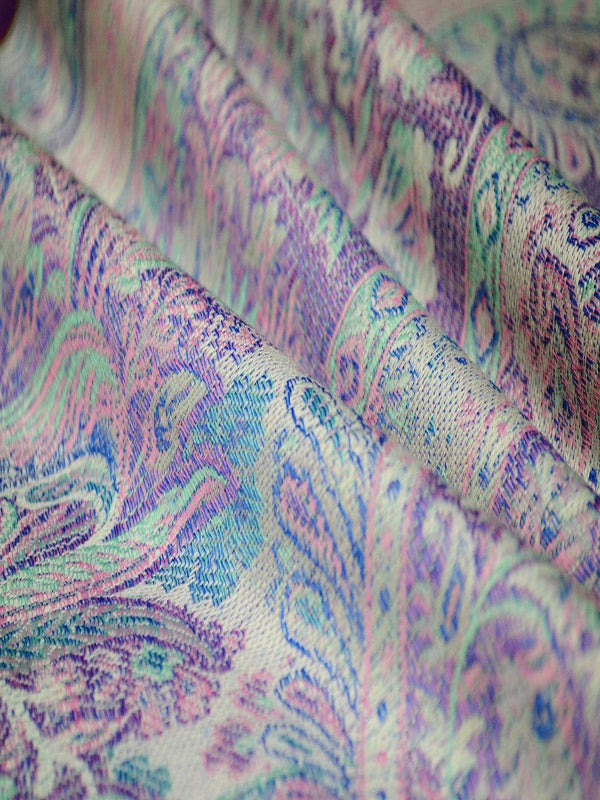 Close-up of a woven Jamawar baby wrap sling in soft pastel hues of lilac, aqua, and mint, showcasing intricate paisley motifs and a breathable wool-blend weave designed for ergonomic for newborn carrying and hands-free parenting.