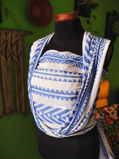 Side angle of Neelanjana woven baby wrap carrier, showcasing layered shoulder fabric, contoured panel, and lightweight cotton weave in blue geometric print, designed for ergonomic babywearing from newborn to toddler.