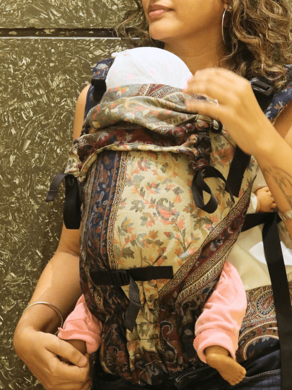 Almitra Tattva Nilofer Yoga ergonomic baby carrier, front carry position with newborn, soft structured carrier with padded straps and adjustable buckles for hands-free parenting in urban setting.