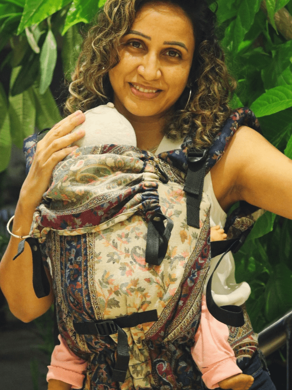 Almitra Tattva Nilofer Yoga newborn carrier outdoors, ergonomic baby carrier with hood and side adjusters, baby held close in front carry for breathable, supportive, gender-neutral babywearing.