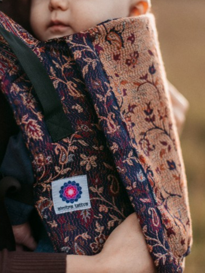Close-up of Sapphire Yoga Baby Carrier featuring handwoven cashmere in deep blue and ochre floral patterns with Almitra Tattva logo.