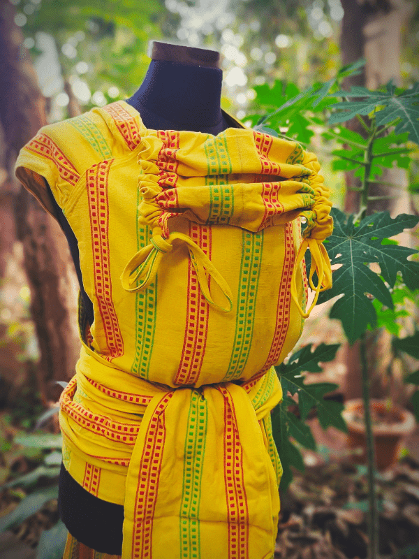 Side angle of the Nima wrap converted Meh Dai carrier with drawstring hood feature and traditional red-green patterned wrap straps, tied securely.