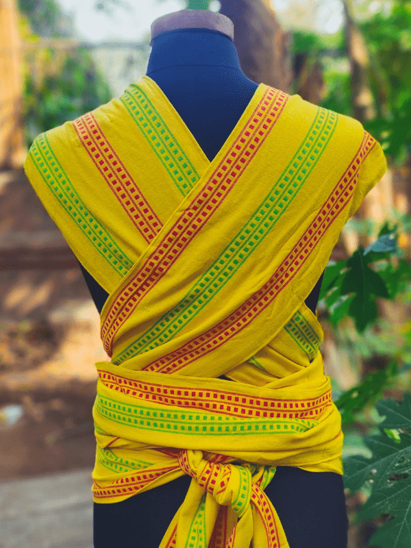 Back view of Nima Meh Dai baby carrier showing criss-crossed wide shoulder straps and supportive wrap tie, in bright yellow with festive Indian stripes.
