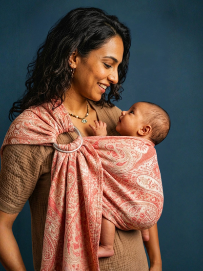Mother smiling down at her infant seated ergonomically inside the Almitra Tattva Tushara ring sling carrier.